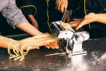 People are using a pasta machine to create fresh pasta, showcasing their culinary skills and team...