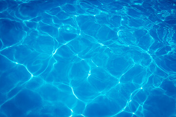 Clear blue swimming pool water surface with sunlight reflections creating abstract patterns and ripples, evoking a refreshing and tranquil summer vibe.