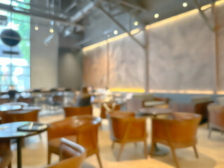 Blurred interior of a modern cafe with wooden chairs and tables, warm lighting, and large windows, creating a cozy and inviting atmosphere for social gatherings and relaxation.