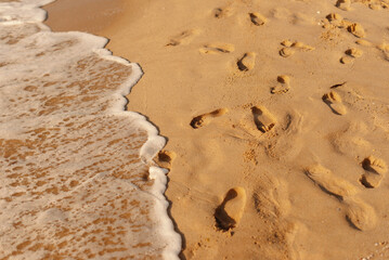 Footprints left in the sandy beach as ocean waves approach, capturing a peaceful coastal moment at sunset.