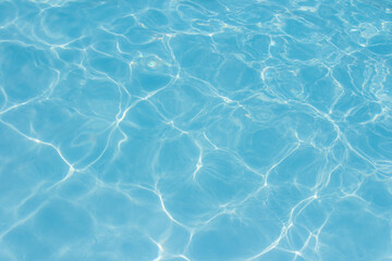 Clear blue swimming pool water surface with sunlight reflections creating abstract patterns and ripples, evoking a refreshing and tranquil summer vibe.