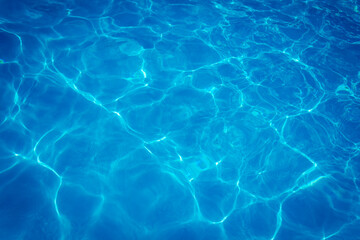 Clear blue swimming pool water surface with sunlight reflections creating abstract patterns and...