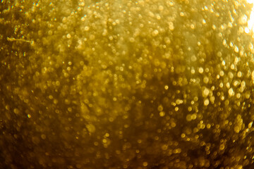 Abstract blurred golden glitter texture with sparkling bokeh lights creating a festive and luxurious background, ideal for holiday and celebration themes.