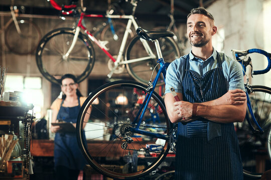 Portrait, man and bicycle repair shop with arms crossed from mechanic, technician and maintenance work. Workshop, thinking and happy business owner with staff and bike for fixing with apron and pride
