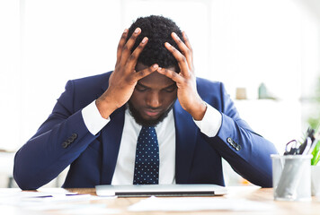 Stressed and overworked black young businessman sitting in office with hand on forehead, copy space