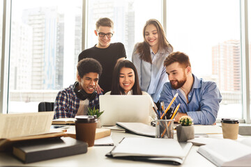 Multiethnic group of individuals gathered in an office setting, all focused on the screen of a...