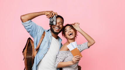 Ready for vacation. Happy couple with suitcase and tickets over pink background
