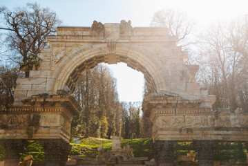 Fototapeta premium In a sunlit forest stands a historic stone arch under a blue sky, blending ancient architecture with natural beauty