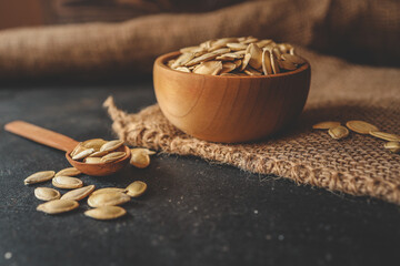 pumpkin seeds in a wooden bowl and vintage scoop. Close up on a black background. copy space for...