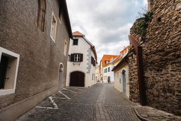 A serene and quiet cobblestone street flanked by historic European buildings, set against a cloudy sky