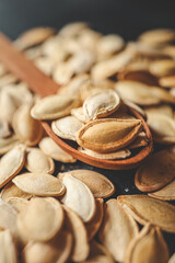 Scattering pumpkin seeds in a wooden spoon on a black background