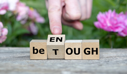 Hand turns wooden cube and changes the expression 'be tough' to ' be enough'.