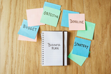 Business Plan Workspace with Notebook and Sticky Notes on Wooden Desk