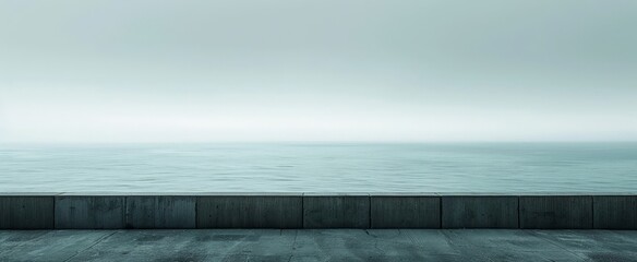 A serene view of the ocean behind a concrete seawall on what appears to be a cloudy day.