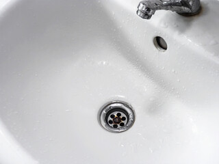 Wash basin with tap faucet. Wet water drops on the white basin in the bathroom. Household plumbing. Cleaning and hygiene. Water down on drainage hole.