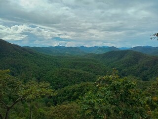 Obraz premium The panoramic landscape view of lush green mountain range covers with rain forest and cloudy rainy day in Chiang Mai, Thailand during rainy season. Small villages settles in the valley.