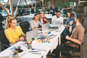 Young designers discussing new project, working on laptops and talking in office, free space