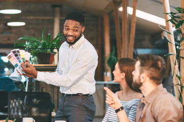 Colleagues discuss and review color swatches in a modern, daylight-filled office, engaging in a creative team meeting.