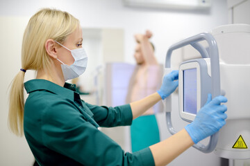 Fototapeta premium Female radiologist is making an Xray of lungs of patient in X-ray room of modern clinic. Doctor performs a fluorography. Medical examination of people is prevention of tuberculosis spread
