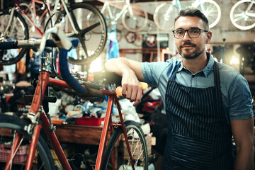 Bicycle, garage and repair shop for man, portrait and small business of mechanic, apron and equipment. Proud, owner and person with service, maintenance and tools for bike, technician and working