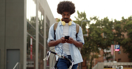 Afro African American man with an urban bike in a city chatting with a smartphone in a city
