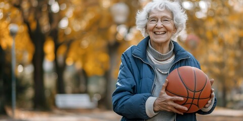 A joyful senior woman holds a basketball and smiles warmly in an autumnal park setting