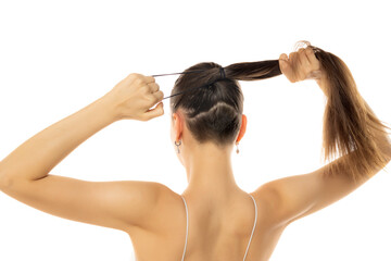 Rear view of a young modern woman with a partially shaved head tying a ponytail on a white background