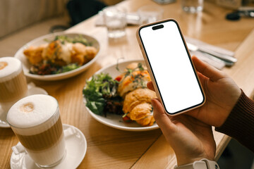 A phone with an isolated screen in hands against the background of breakfast in a cafe, an application for counting calories
