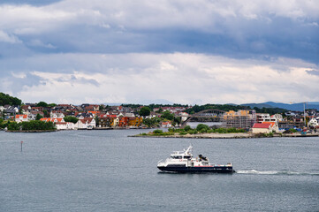 A small car ferry sails between stops in Stavanger, southern Norway, on a cloudy spring day. The sea is very calm