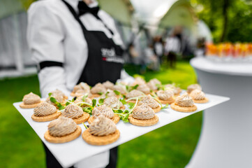 Close-up view of a tray with neatly arranged canapés held by a person in a black and white...