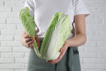 Woman separating leaf from fresh Chinese cabbage near white brick wall, closeup