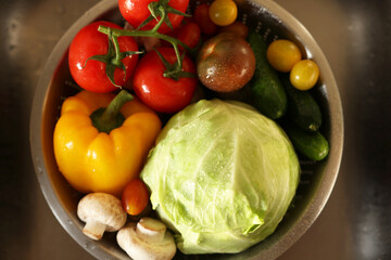 Different wet vegetables in metal colander inside sink, top view