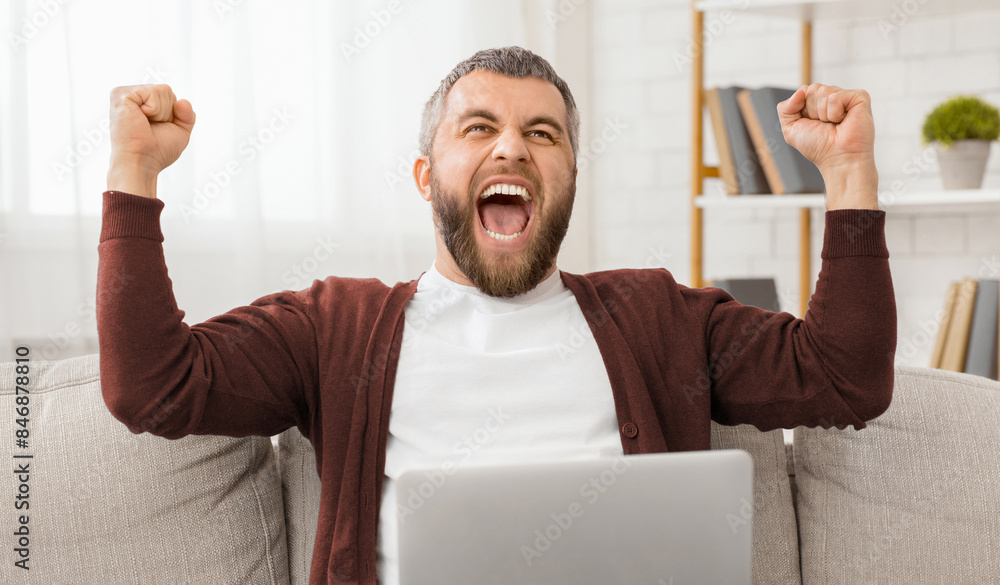 Aufkleber a man is seen sitting on a couch with laptop and his arms raised in the air. he appears to be energe