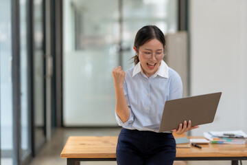 Excited businesswoman celebrates success while working on a laptop in a modern office setting.