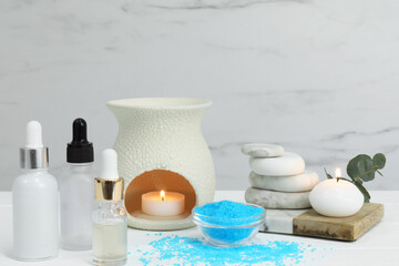 Different aromatherapy products and burning candles on white wooden table
