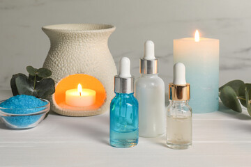 Aromatherapy products and burning candles on white wooden table