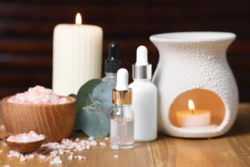 Different aromatherapy products, burning candles and eucalyptus leaves on wooden table