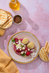 Healthy raw summer vegan snack plate. Flat-lay of beetroot humus dip with falafel and colorful fresh vegetables and greens on pink table background, top view. Clean eating, dieting, vegan