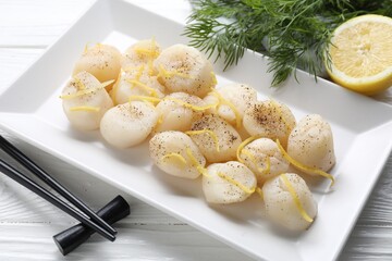 Raw scallops with milled pepper, lemon zest and dill on white wooden table, closeup
