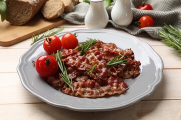 Slices of tasty fried bacon with rosemary and tomatoes served on wooden table
