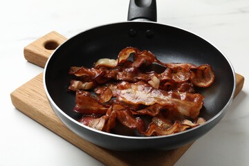 Delicious bacon slices in frying pan on white table, closeup