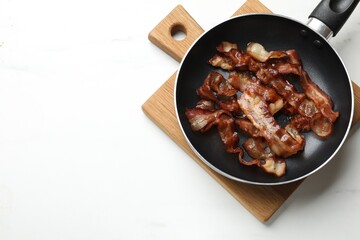 Delicious bacon slices in frying pan on white marble table, top view. Space for text