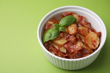 Delicious baked potatoes, bacon and basil in bowl on green background, closeup. Space for text