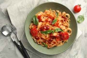 Delicious pasta with tomato sauce and basil served on grey textured table, flat lay