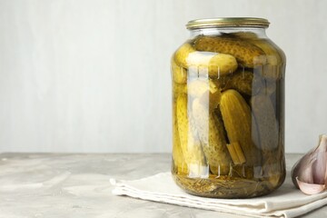 Pickled cucumbers in jar and garlic on grey table. Space for text