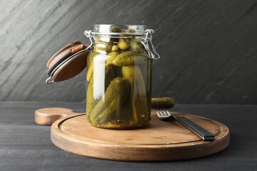 Pickled cucumbers in jar and fork on grey wooden table