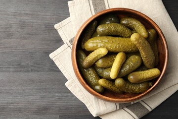 Pickled cucumbers in bowl on grey wooden table, top view