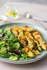 Fried zucchini flowers in batter and mix salad with cucumbers close up
