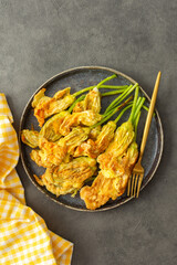 Fried zucchini flowers in batter, a plate with zucchini flowers on a dark background, top view