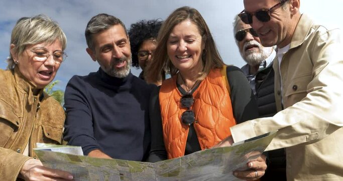 Group of diverse middle aged friends looking at a map during vacation in a city 